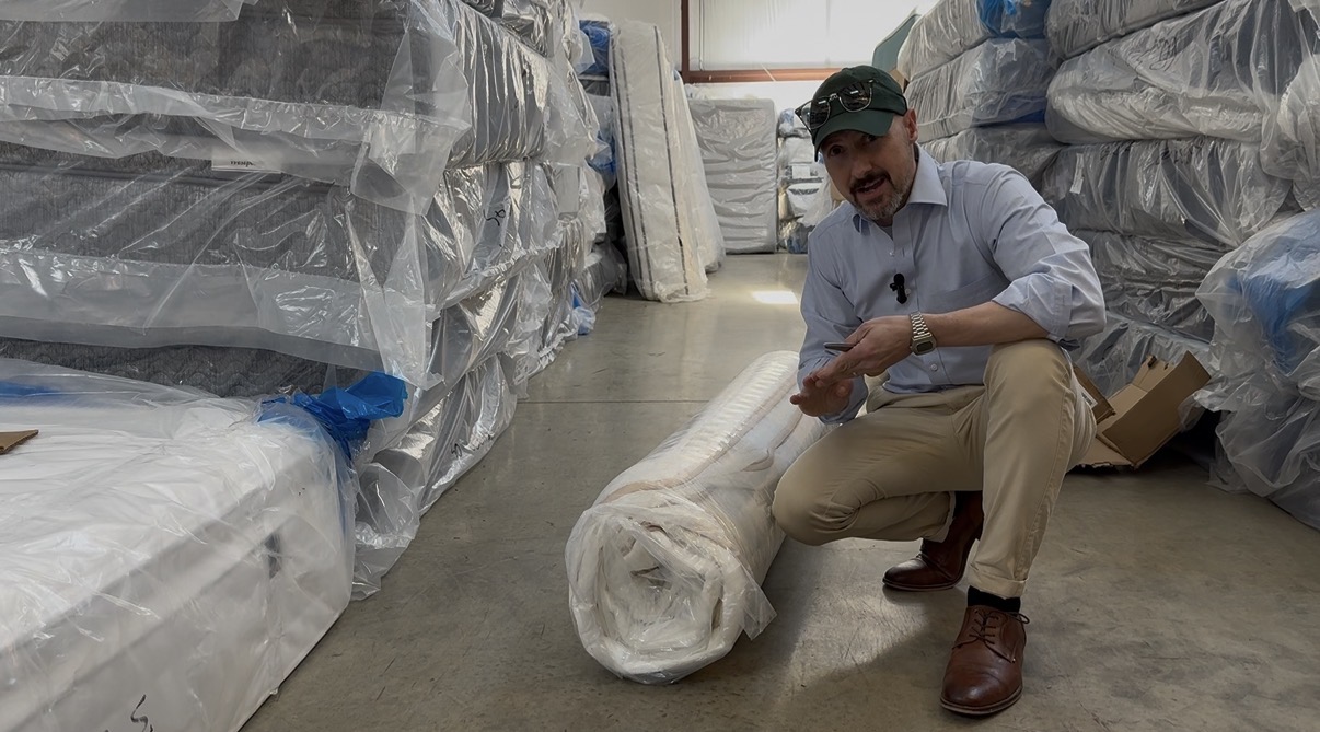Cut open bed-in-a-box hybrid mattress showing weak coils, low-density foam layers, and minimal edge support compared to a commercial-grade store-bought mattress.
